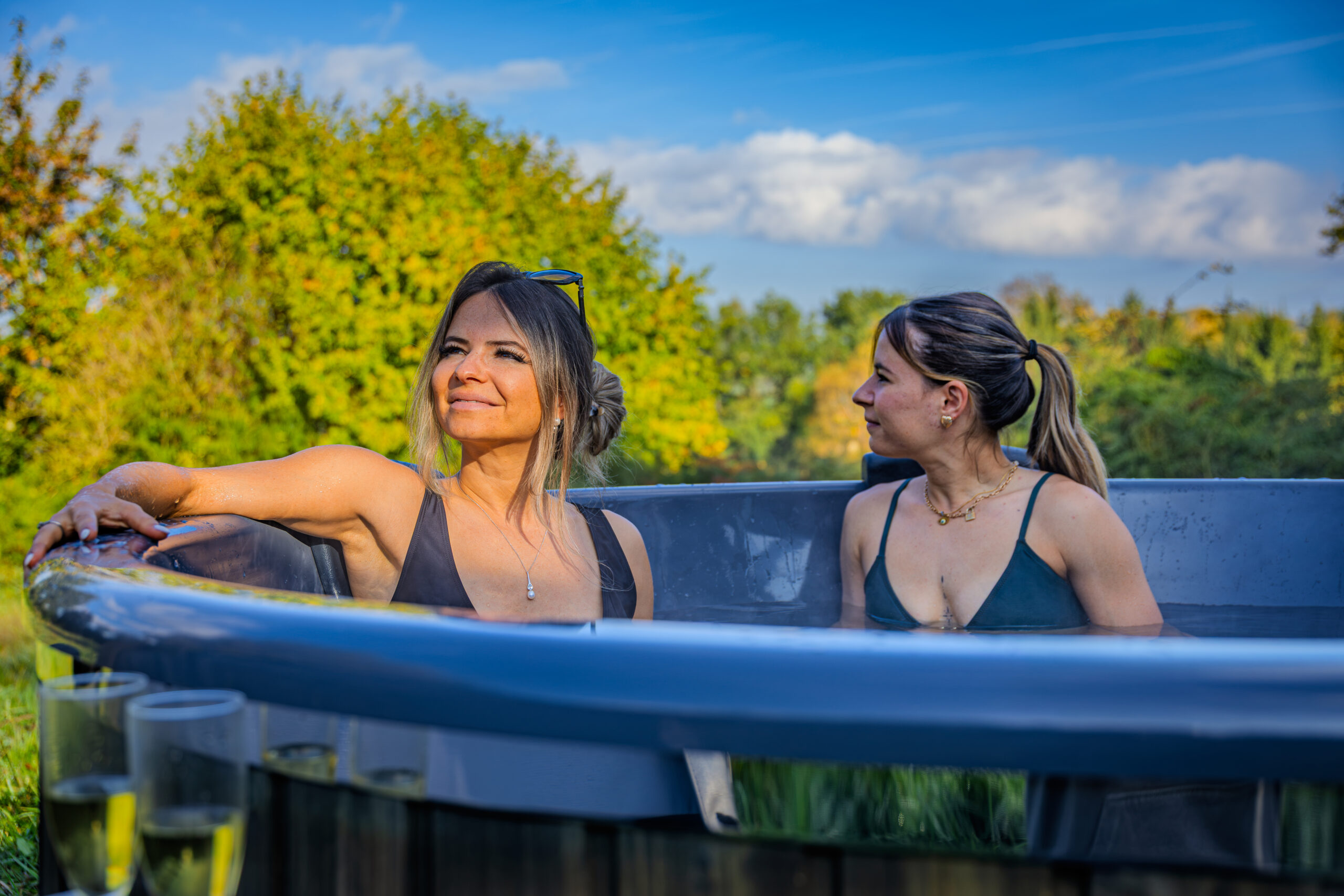 Deux femmes se détendent avec des coupes de champagne dans le bain nordique extérieur d'un lodge Les Hauts du Val