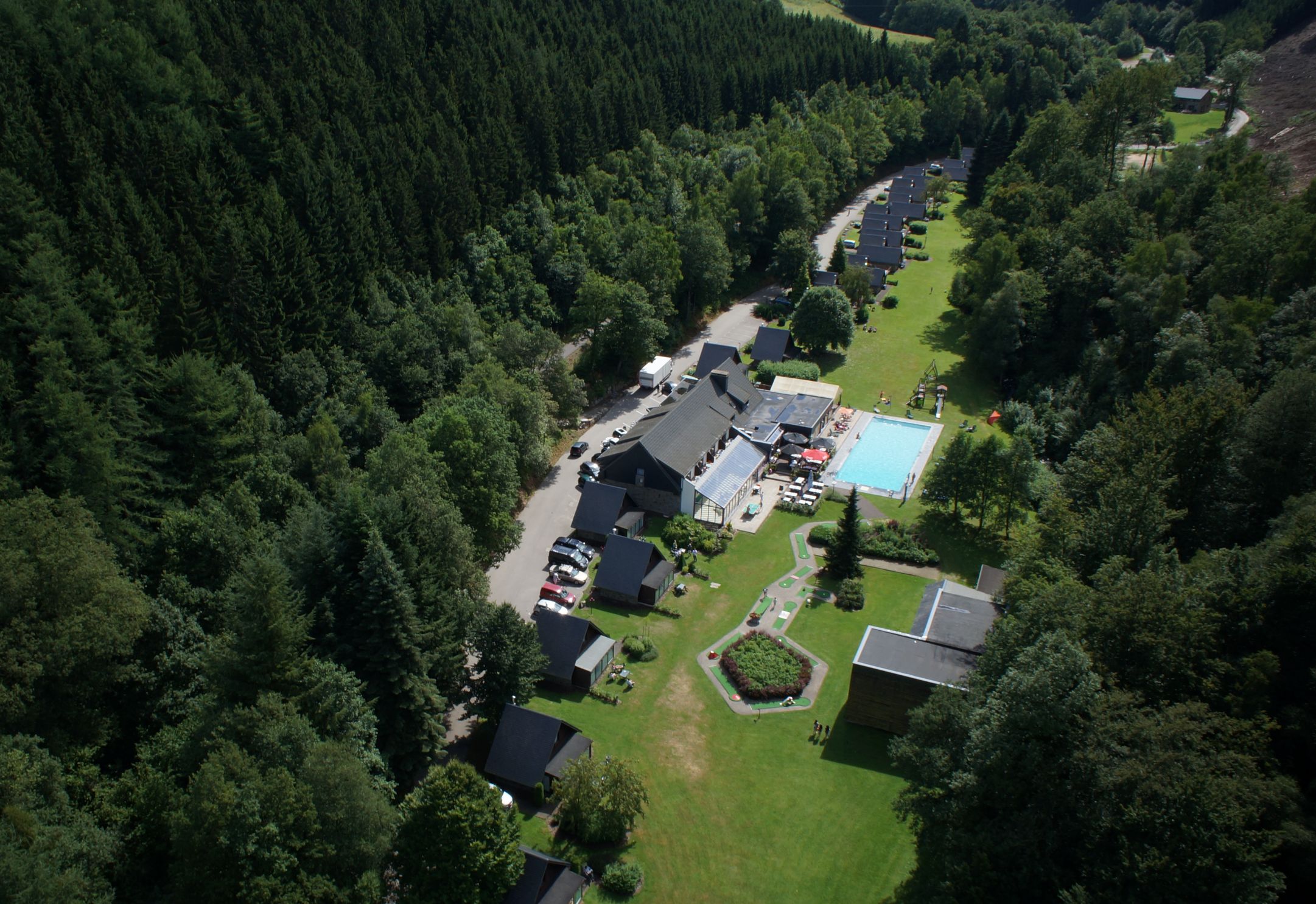 Vue aérienne du domaine du Val d'Arimont à Malmedy, bâtiments et piscine nichés dans la vallée boisée des Ardennes